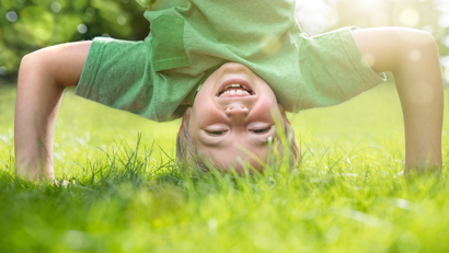 Happy boy doing a headstand on the grass in the summer