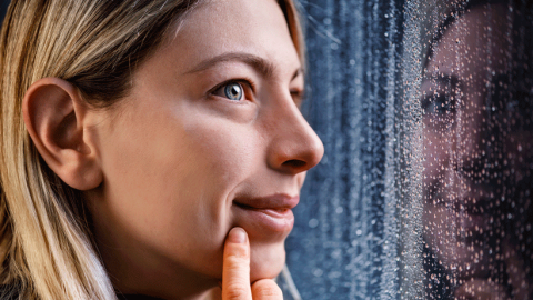 Thoughtful blonde woman looking out of a rainy window