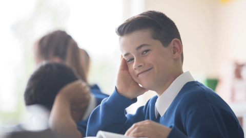 Close-up of primary school boy wearing a blue and white uniform in a classroom, looking assured.