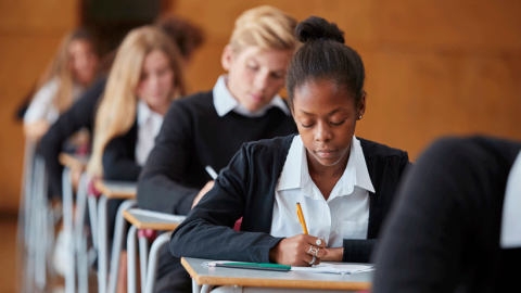 Photo of mixed ethnicity teenage students in navy uniforms sitting exams in a school hall.