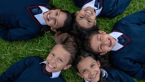 Five school pupils lying on the grass looking happy and relaxed