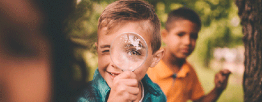 Little boy outside looking through magnifying glass