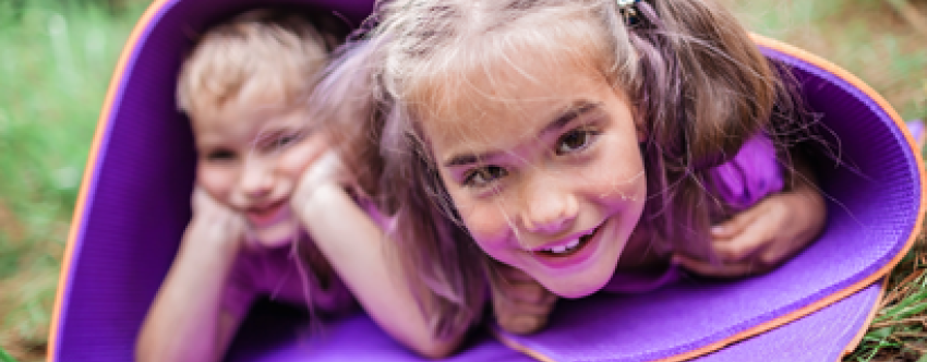 Happy boy and girl playing in a rolled up purple yoga mat outside