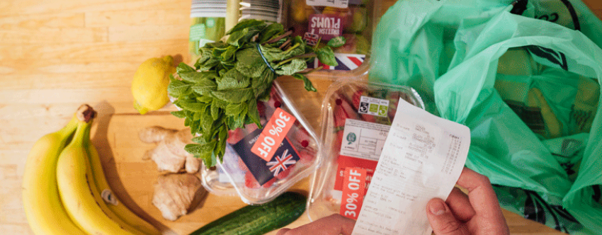 Photo of small pile of groceries with person's hand suggesting they are scrutinising the shopping receipt.