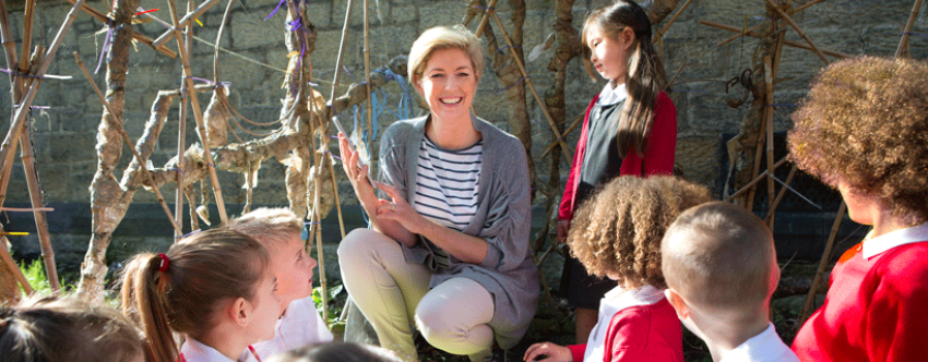 Female teacher and primary school pupils in an outdoor learning space in the school playground.